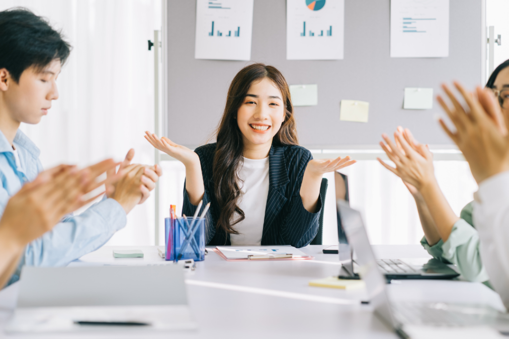 หญิงสาวผู้นำเสนอในห้องประชุมได้รับเสียงปรบมือจากทีมงานหลังการนำเสนอโครงการสำเร็จ